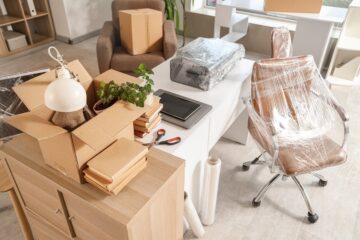 interior of office with desk, boxes and wrapped chairs in stretch film on moving day