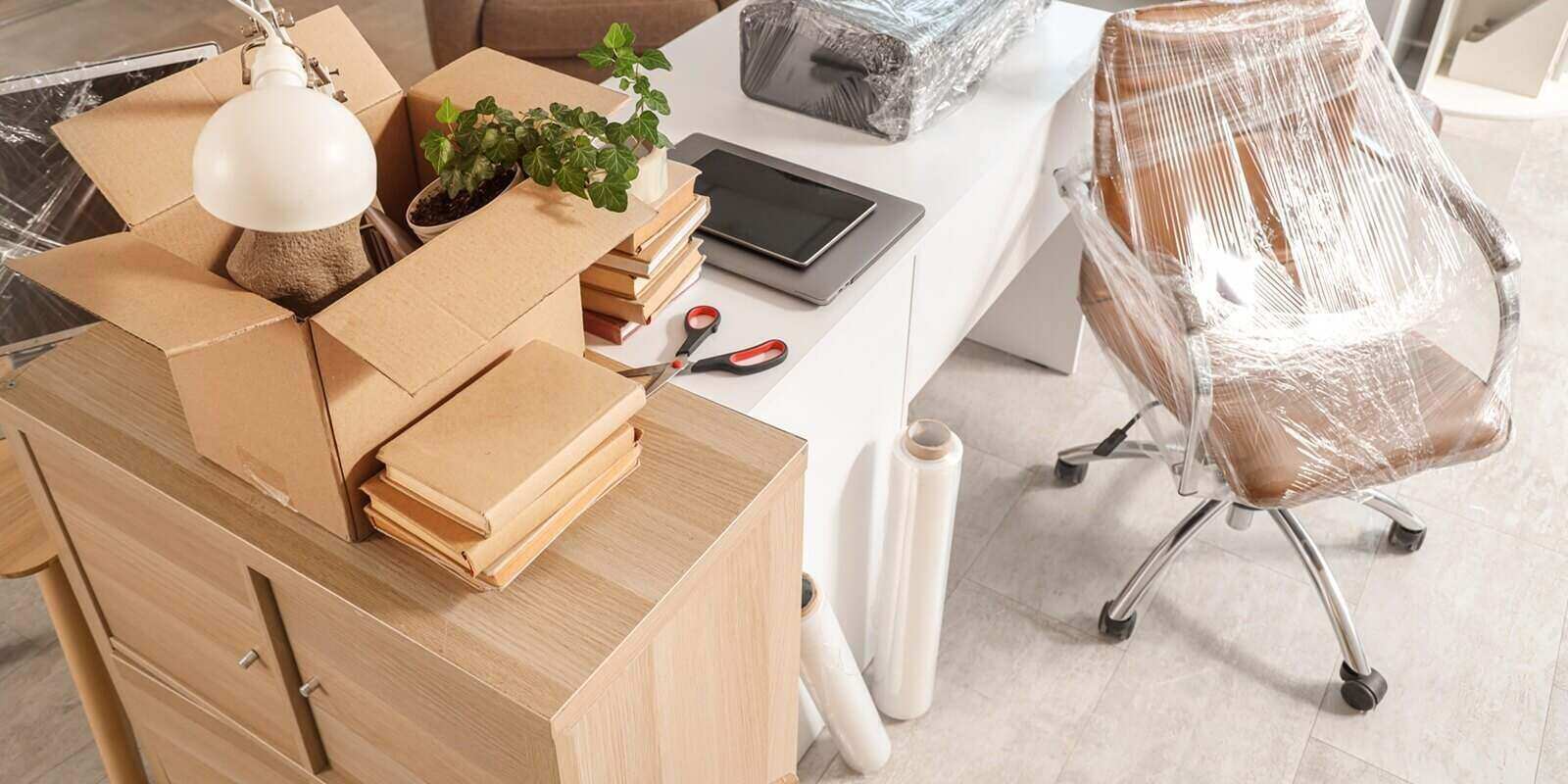 interior of office with desk, boxes and wrapped chairs in stretch film on moving day