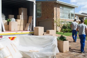 movers carrying boxes from moving van in sunny driveway