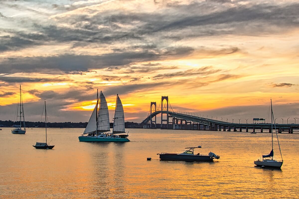 sailboats at rest in Newport Rhode Island harbor as a peaceful sun sets behind the Newport bridge